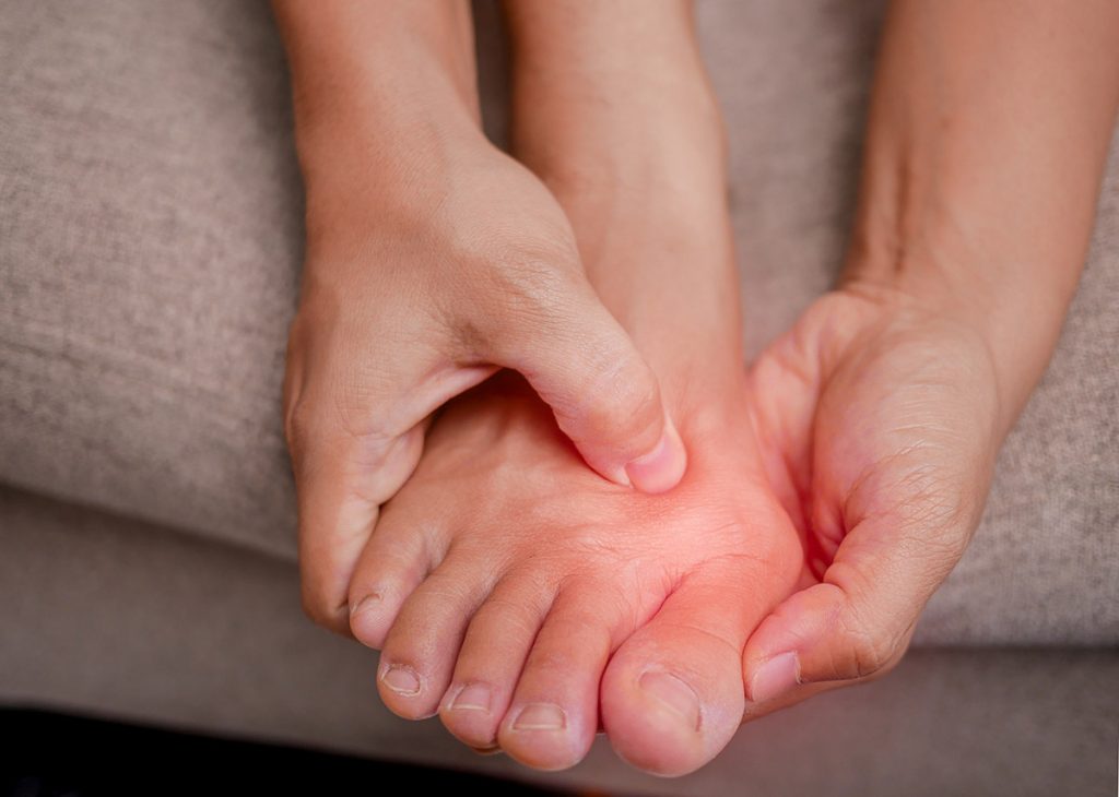 A person holding their foot near their toe joint in pain.